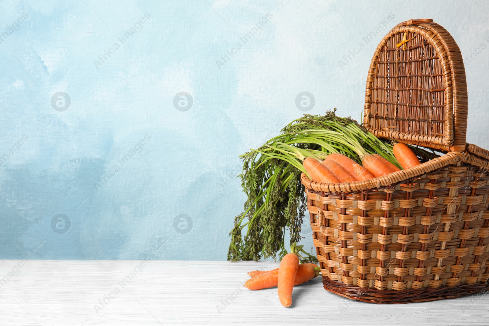 Photo of Wicker basket with ripe carrots on table