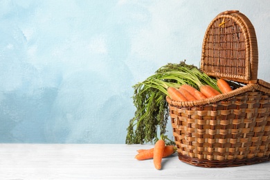 Wicker basket with ripe carrots on table