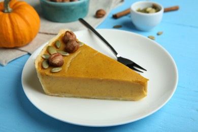 Photo of Piece of delicious pumpkin pie with hazelnuts, seeds and fork on light blue wooden table
