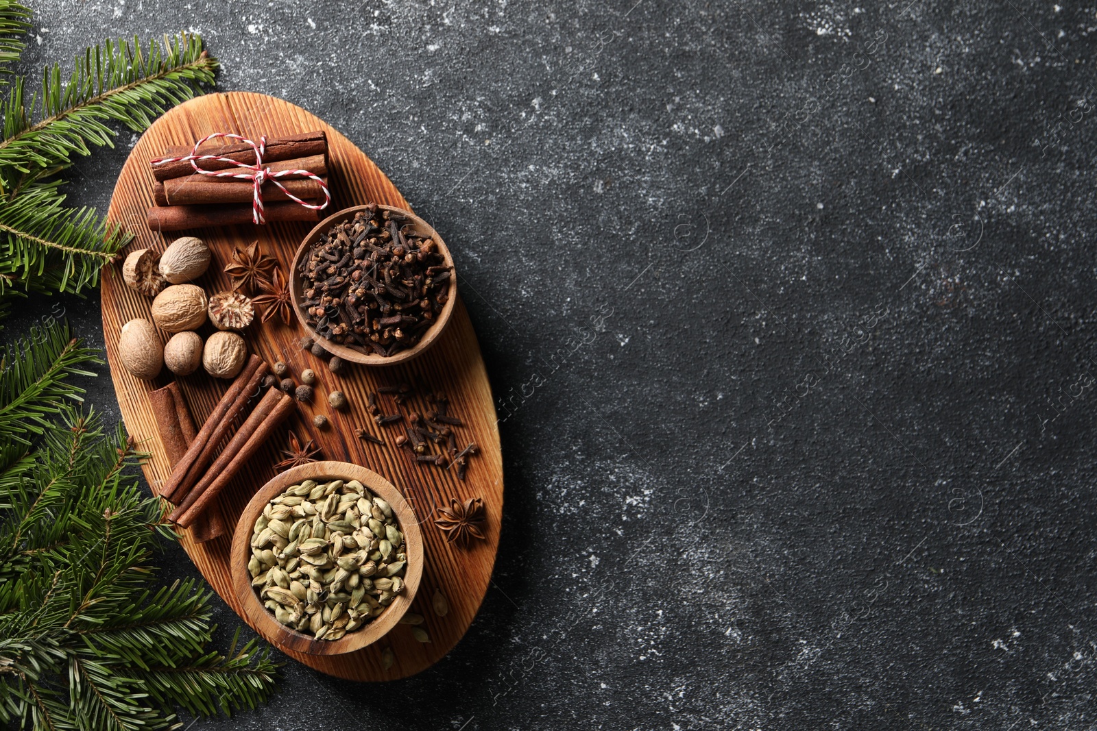 Photo of Different spices and fir branches on dark gray table, flat lay. Space for text
