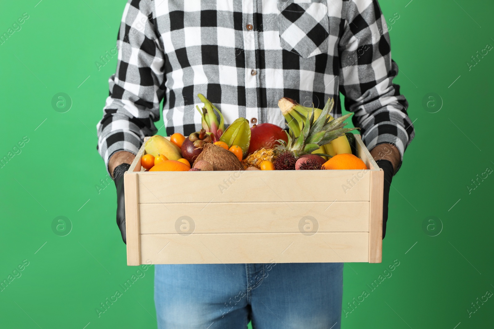 Photo of Courier holding crate with assortment of exotic fruits on green background, closeup