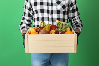 Courier holding crate with assortment of exotic fruits on green background, closeup