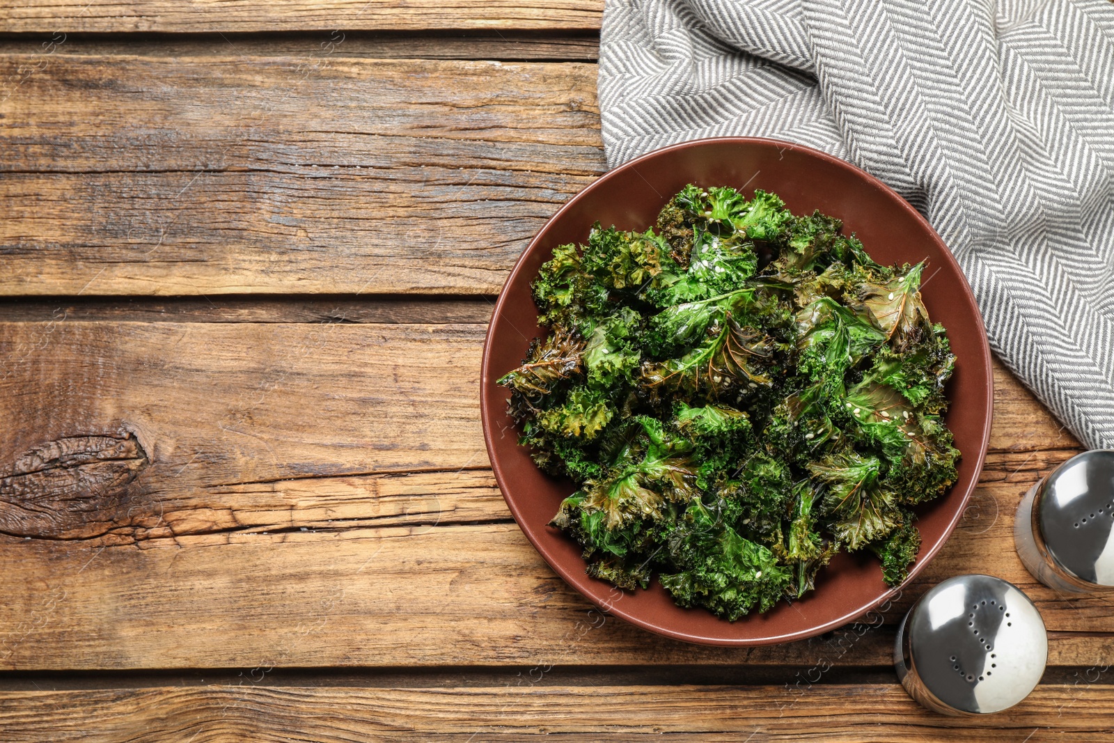 Photo of Tasty baked kale chips on wooden table, flat lay. Space for text