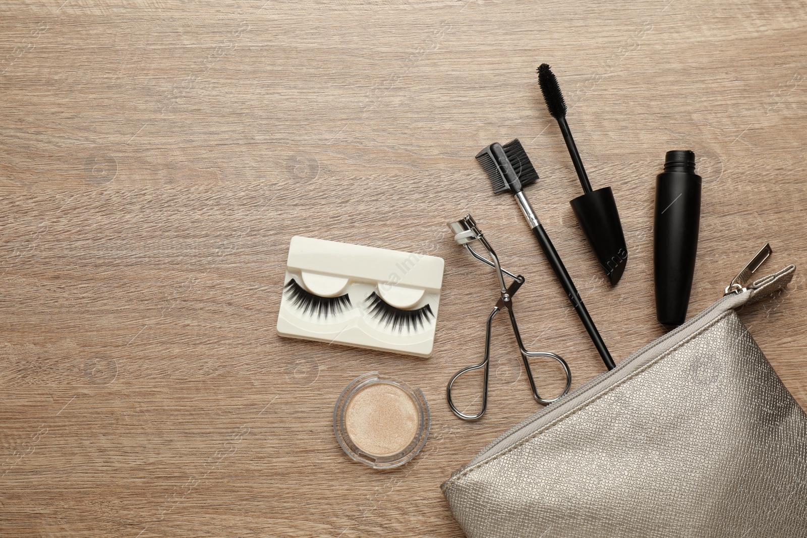 Photo of Flat lay composition with eyelash curler, cosmetic bag and makeup products on wooden table. Space for text