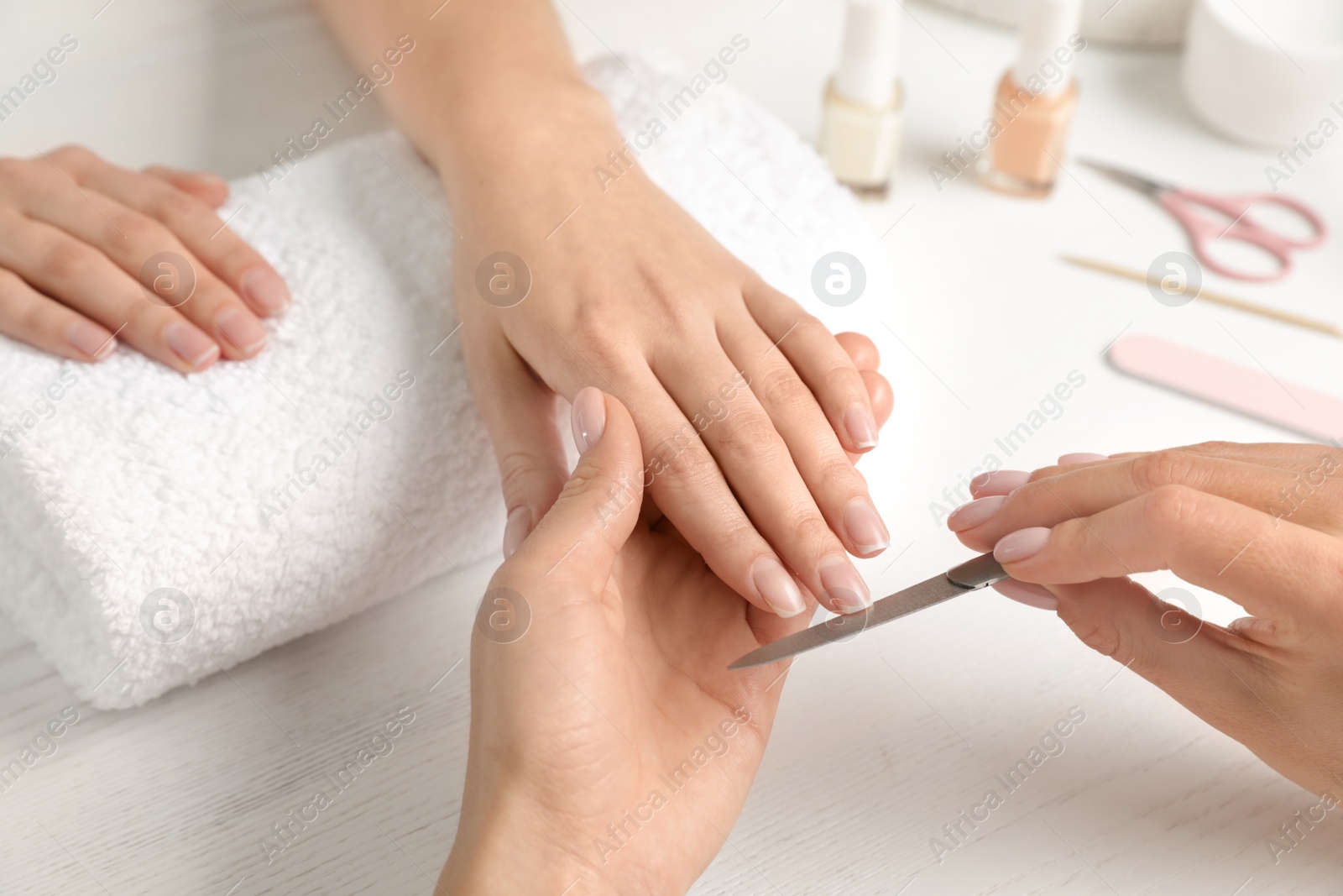 Photo of Manicurist filing client's nails at table, closeup. Spa treatment