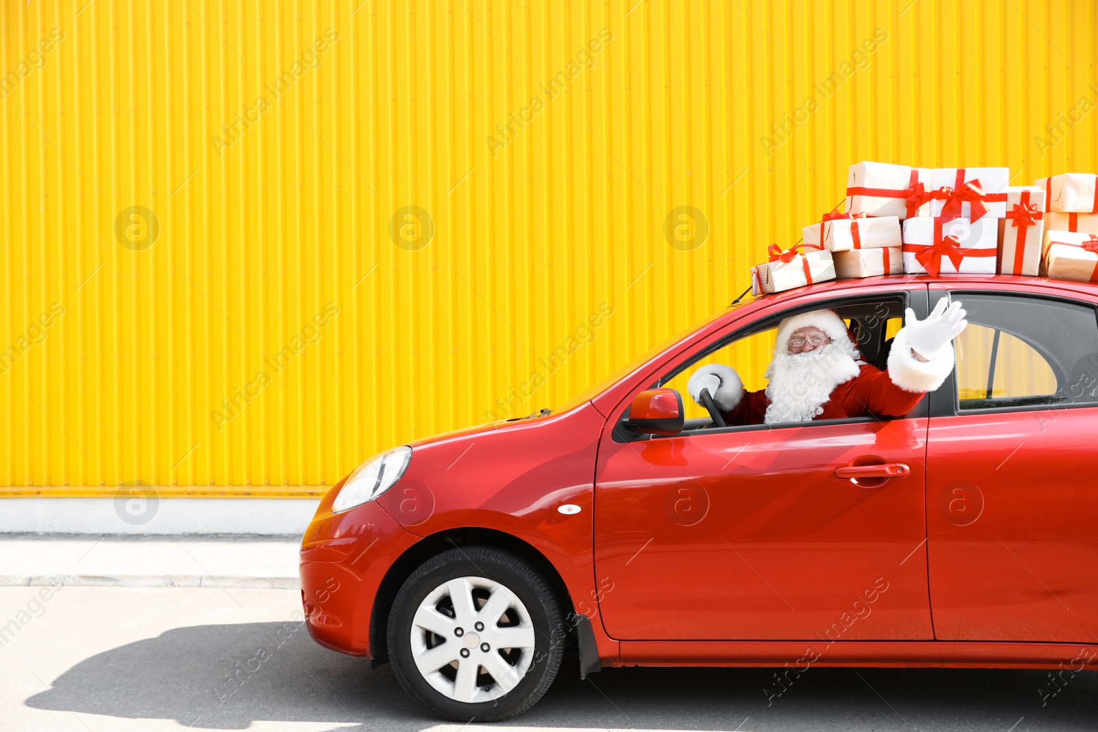 Photo of Authentic Santa Claus driving red car with gift boxes, view from outside