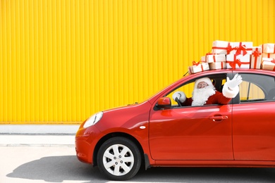 Authentic Santa Claus driving red car with gift boxes, view from outside