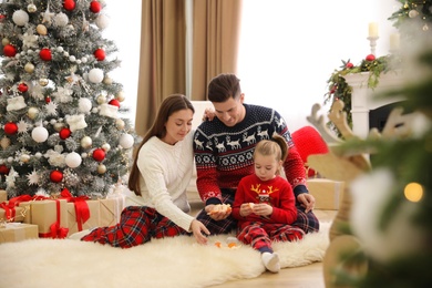 Family with little daughter peeling tangerines in room decorated for Christmas