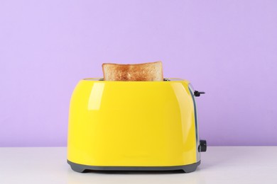 Photo of Modern toaster with slice of bread on white wooden table