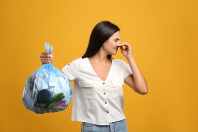 Woman holding full garbage bag on yellow background