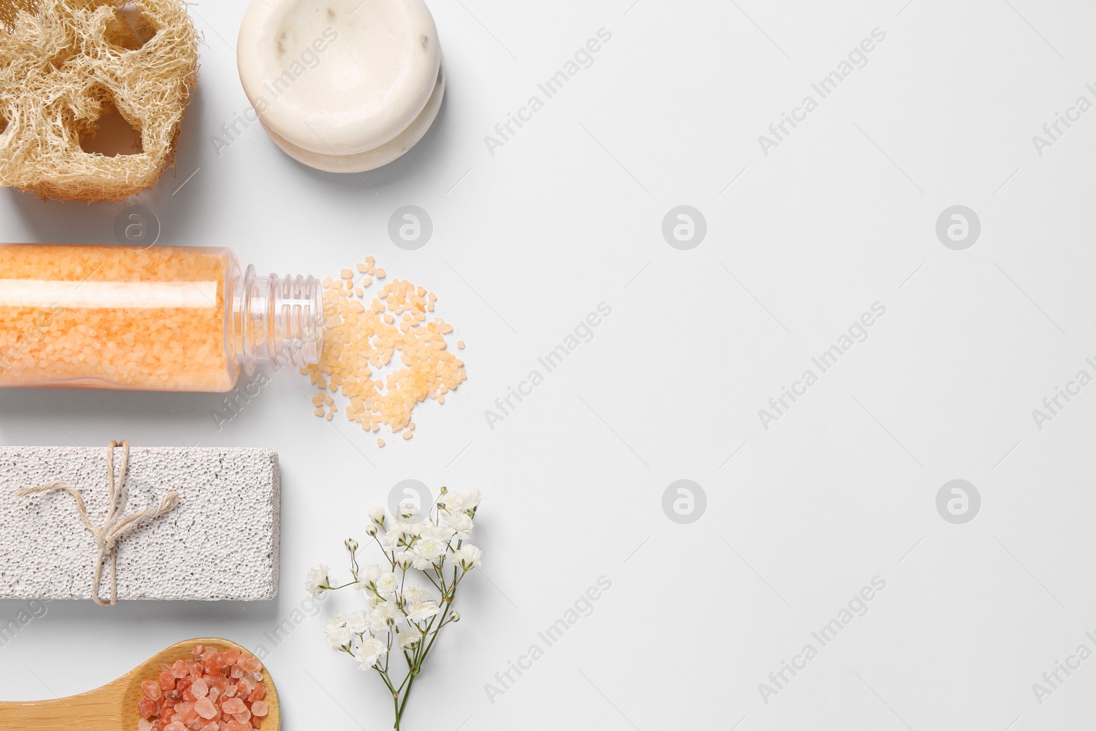 Photo of Sea salt, soap bar, beautiful flowers and loofah on white background, flat lay. Space for text