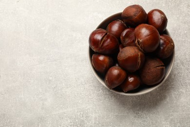 Fresh edible sweet chestnuts in bowl on grey table, top view. Space for text