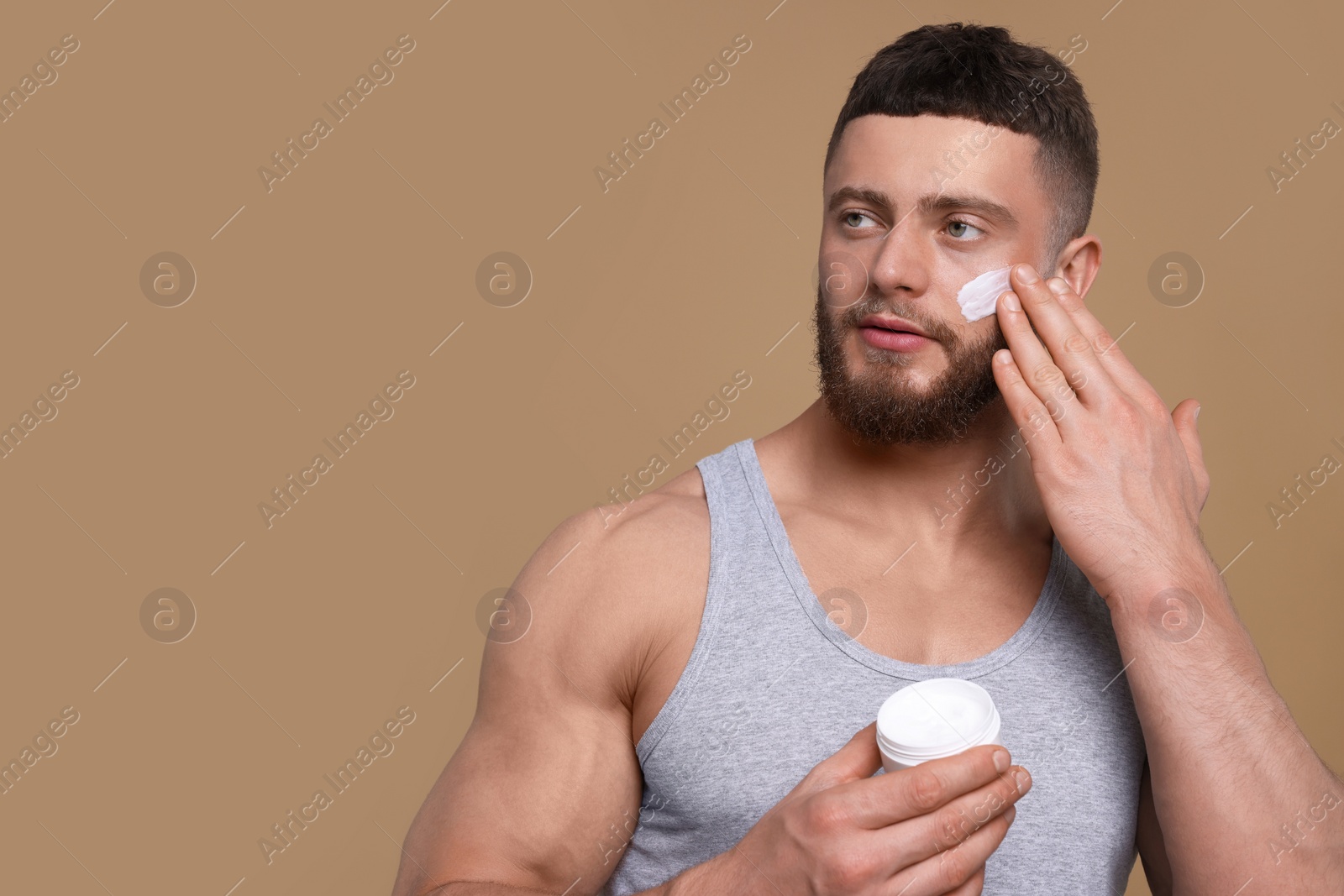 Photo of Handsome man applying cream onto his face on pale brown background, space for text