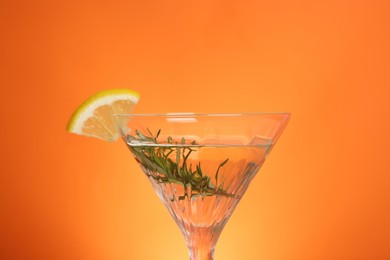 Photo of Martini glass of refreshing cocktail with lemon slice and rosemary on orange background, closeup