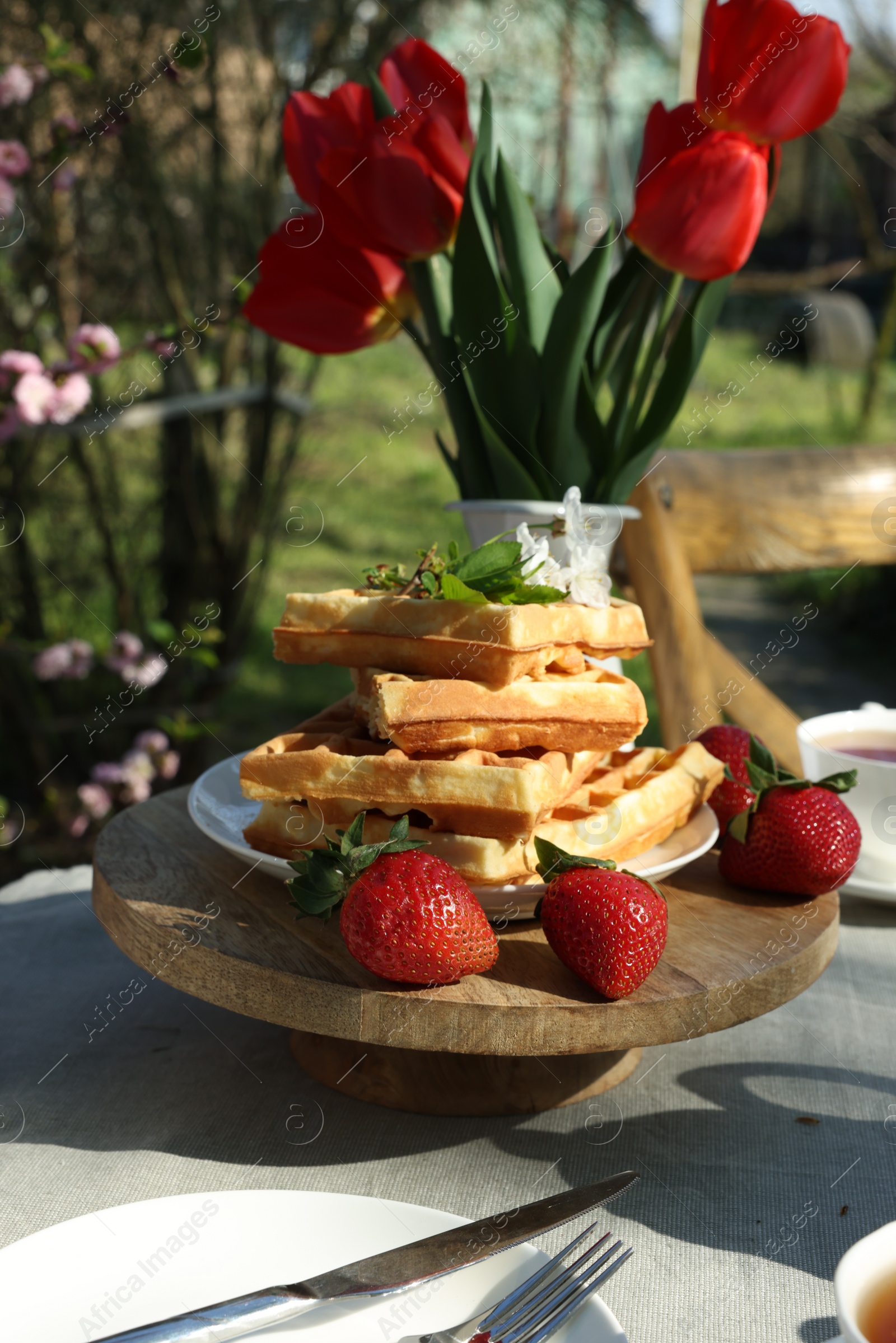 Photo of Freshly baked waffles and beautiful bouquet of tulips on table in garden