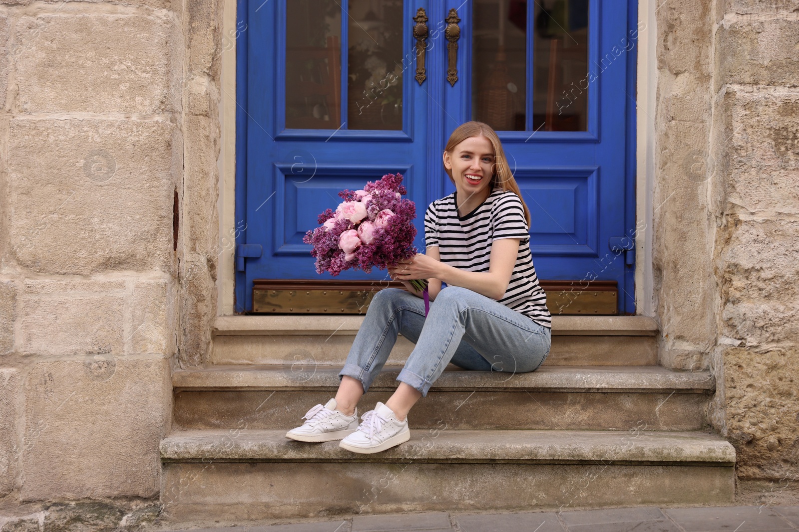 Photo of Beautiful woman with bouquet of spring flowers on stairs near building