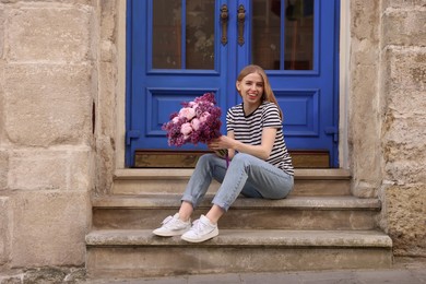 Beautiful woman with bouquet of spring flowers on stairs near building