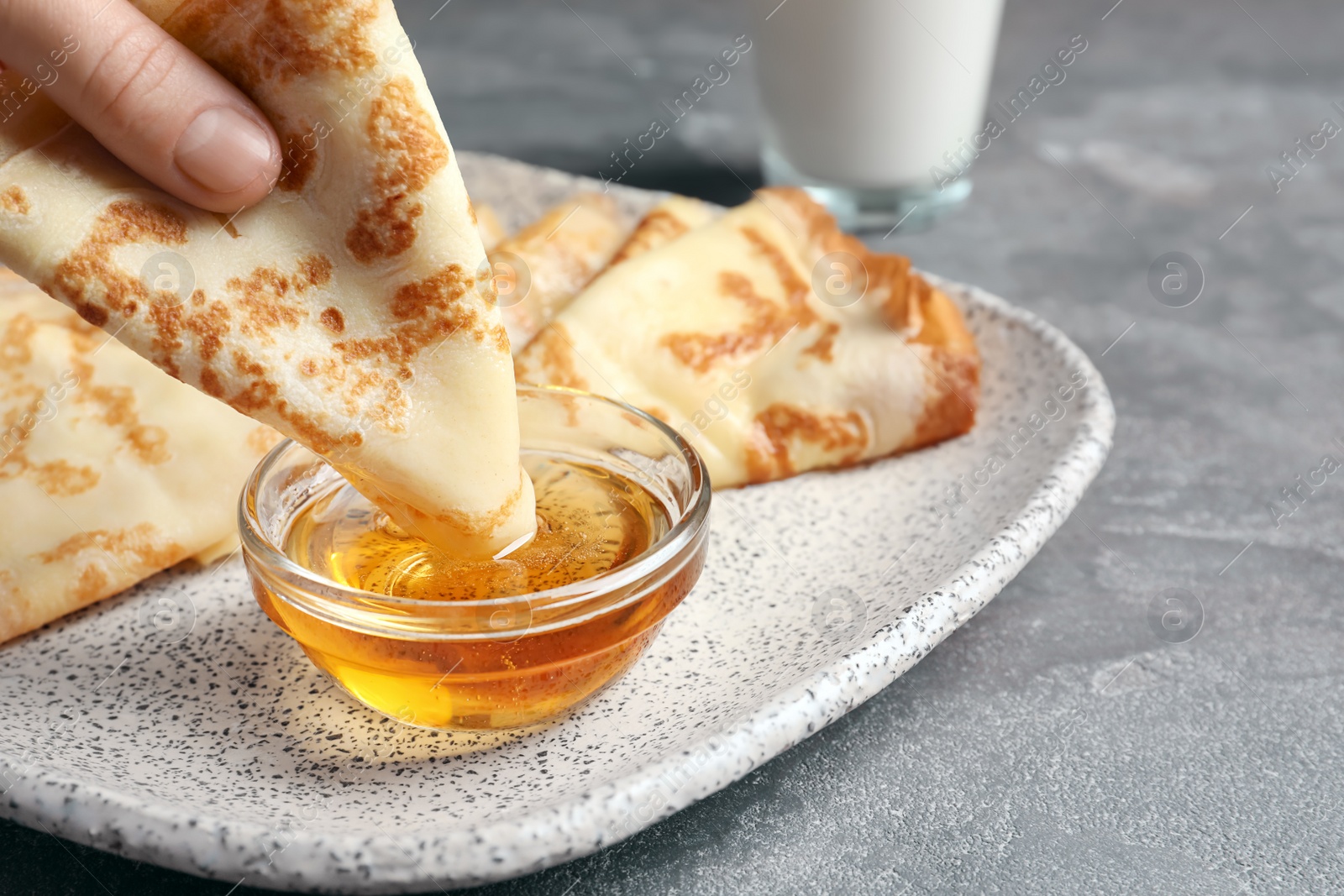 Photo of Woman dipping thin pancake into bowl with honey, closeup