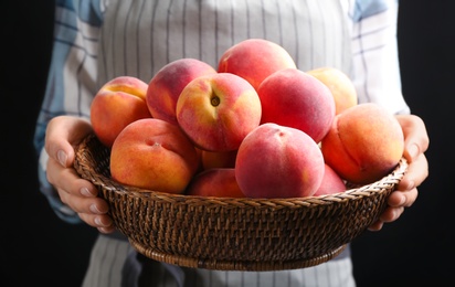 Photo of Woman with fresh sweet peaches in wicker bowl, closeup