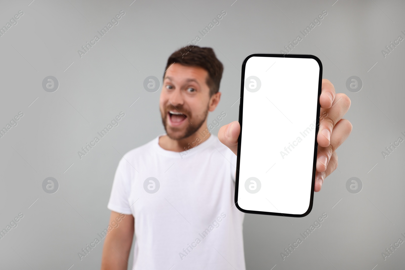 Photo of Surprised man showing smartphone in hand on light grey background, selective focus. Mockup for design