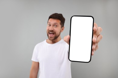 Surprised man showing smartphone in hand on light grey background, selective focus. Mockup for design