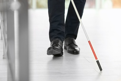 Photo of Blind person with long cane walking indoors, closeup