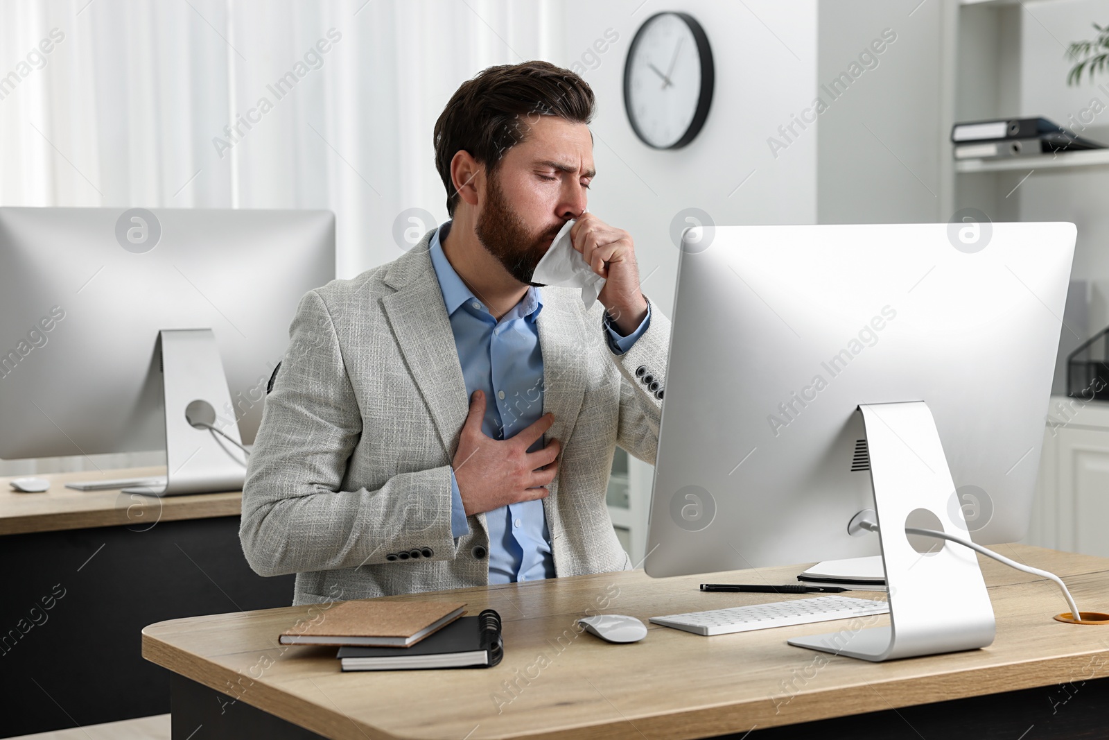 Photo of Sick man with tissue coughing at workplace in office