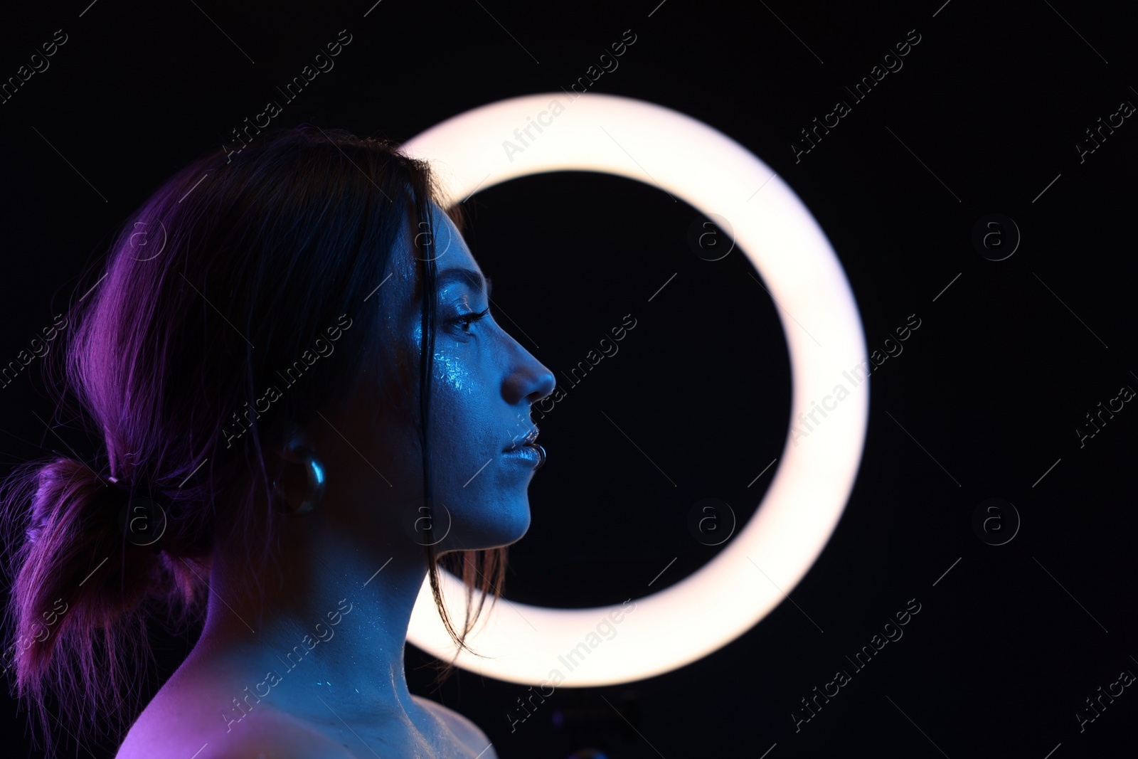 Photo of Beautiful woman and ring lamp on dark background in neon lights