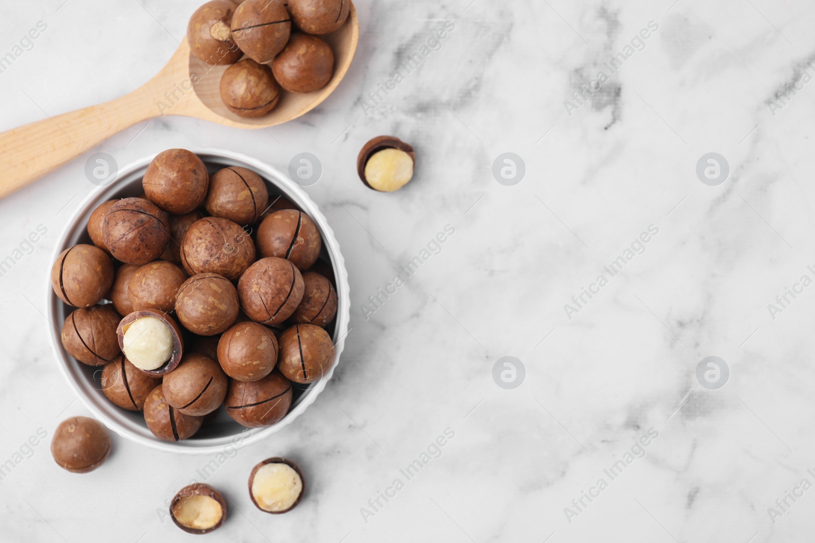 Photo of Tasty Macadamia nuts on white marble table, flat lay. Space for text