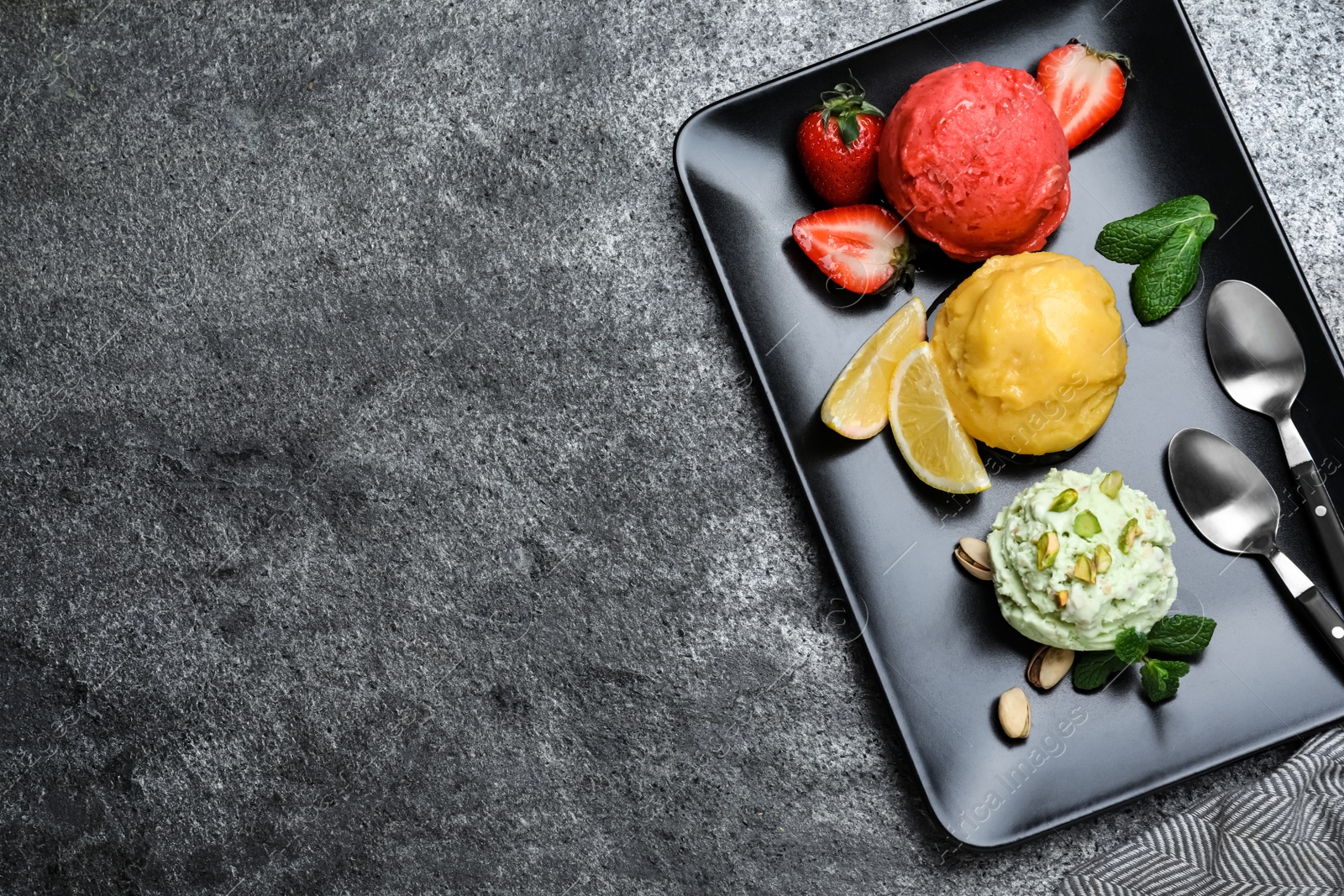Photo of Strawberry, lemon and pistachio ice cream scoops served on grey table, top view. Space for text