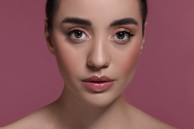 Photo of Portrait of beautiful young woman with perfect makeup on dark pink background, closeup