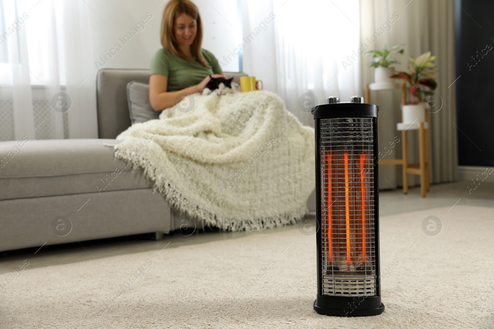 Photo of Woman with cat at home, focus on electric halogen heater