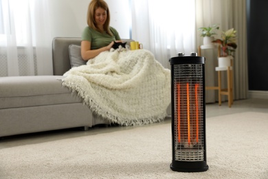 Photo of Woman with cat at home, focus on electric halogen heater
