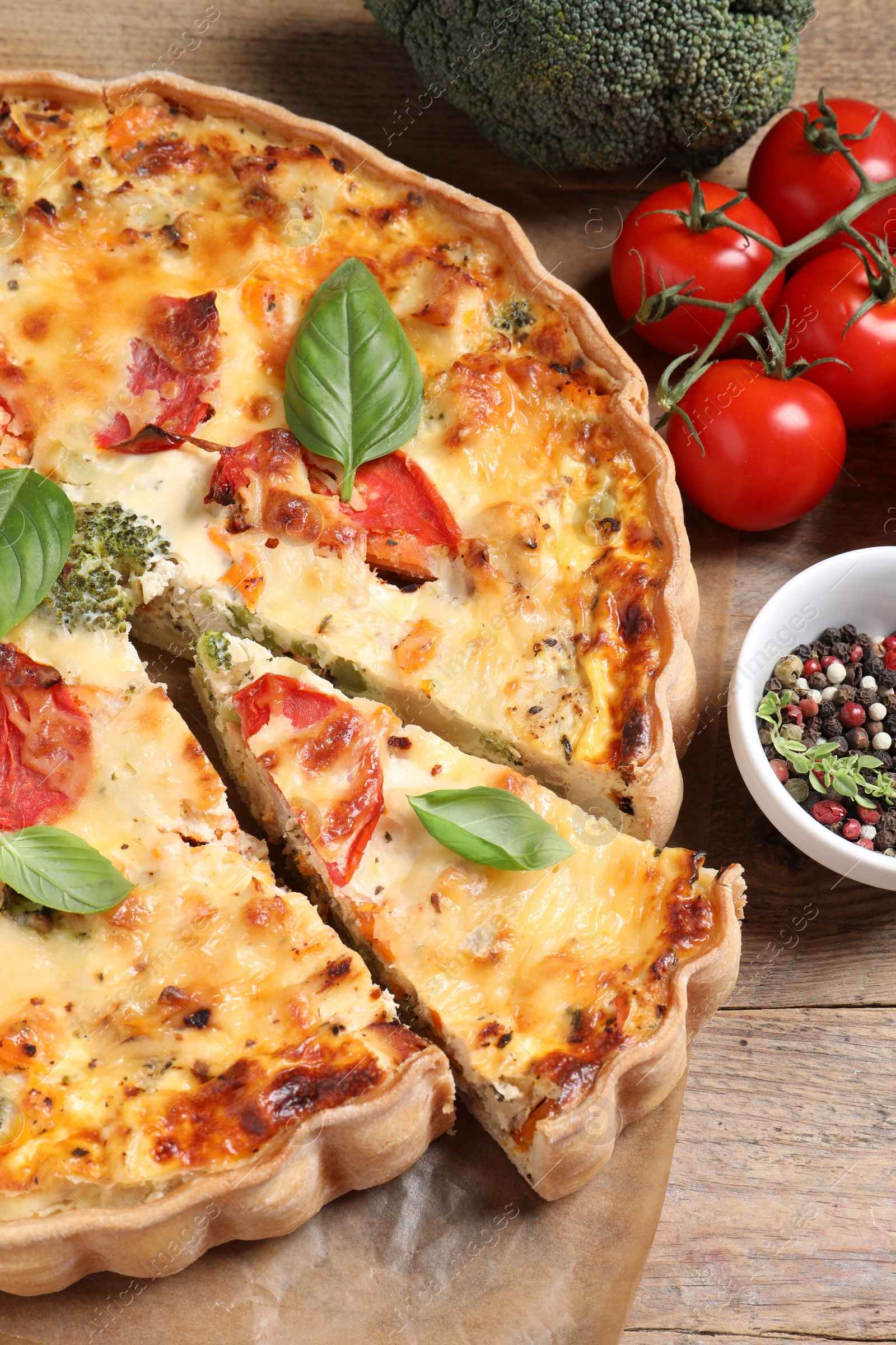 Photo of Tasty quiche with tomatoes, basil and cheese served on wooden table, above view