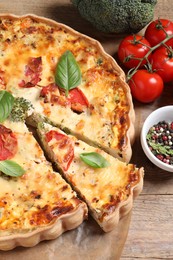 Photo of Tasty quiche with tomatoes, basil and cheese served on wooden table, above view