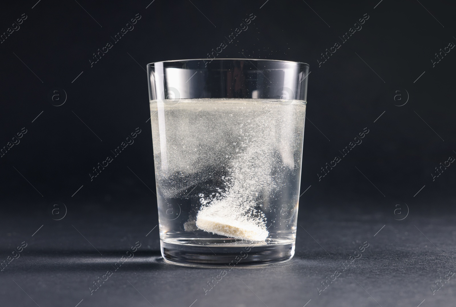 Photo of Effervescent pill dissolving in glass of water on grey table