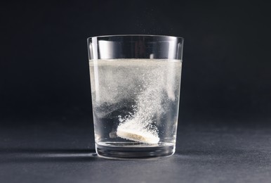 Effervescent pill dissolving in glass of water on grey table