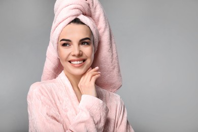 Happy young woman in bathrobe with towel on head against light grey background, space for text. Washing hair