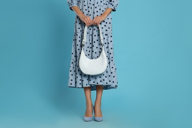 Woman with stylish bag on light blue background, closeup