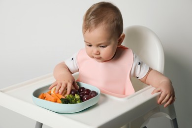 Photo of Cute little baby wearing bib while eating on white background