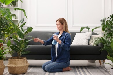 Woman spraying beautiful potted houseplants with water at home