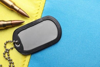 Military ID tag and bullets on Ukrainian flag, flat lay. Space for text