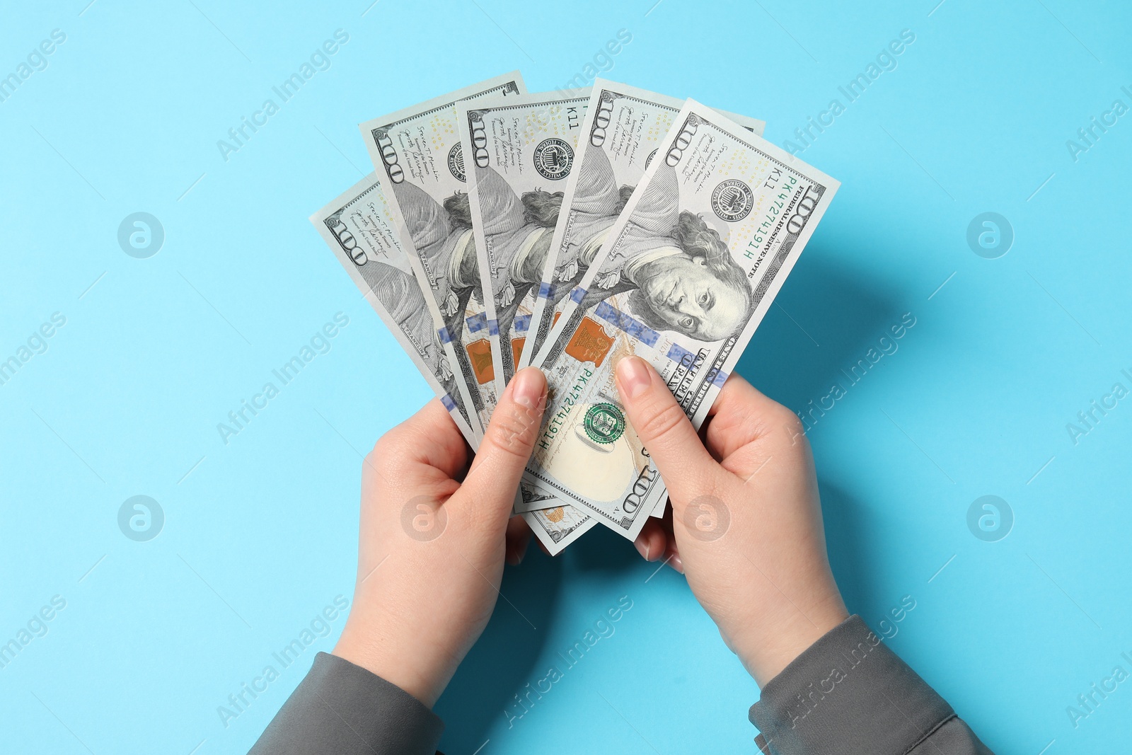 Photo of Money exchange. Woman holding dollar banknotes on light blue background, top view