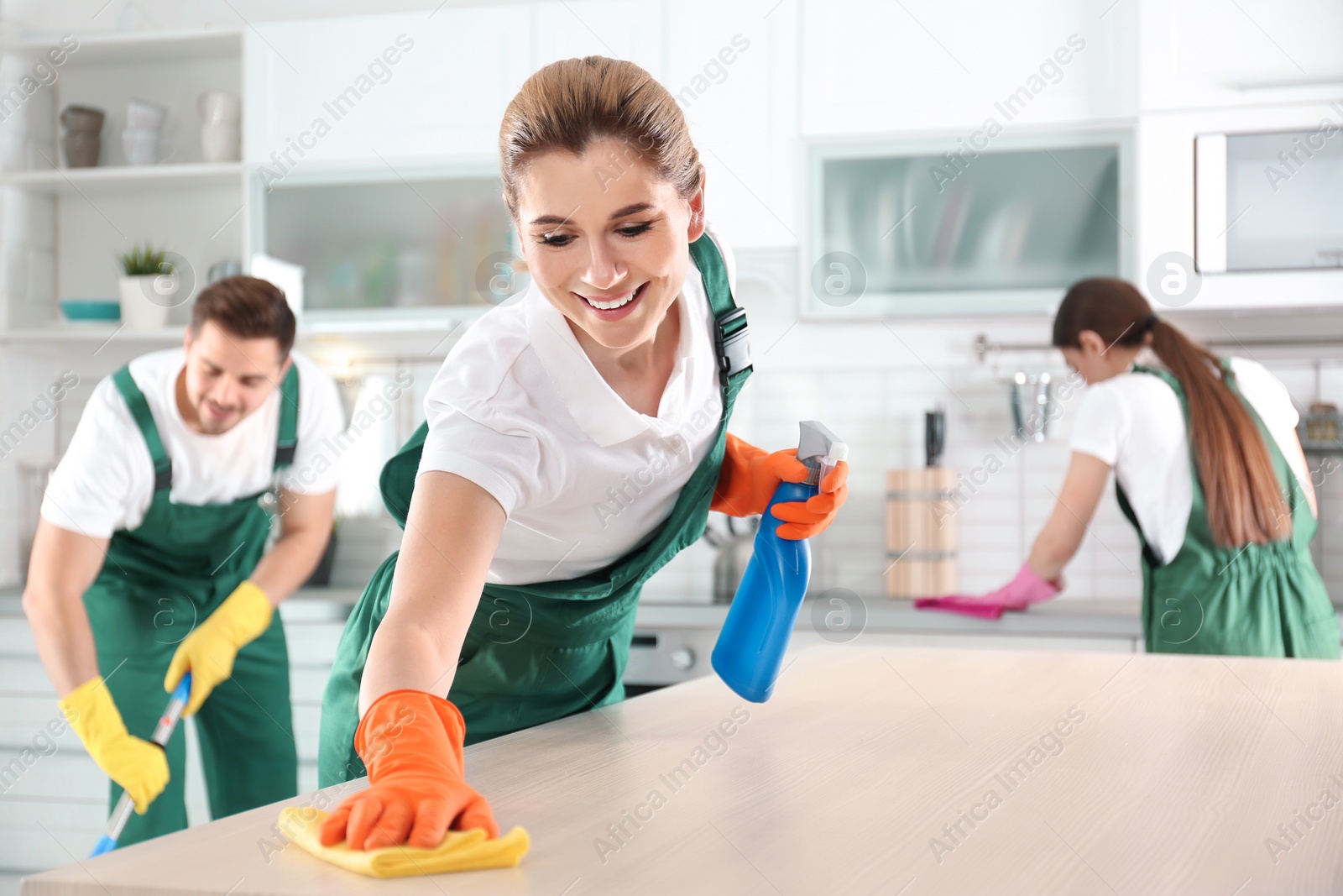 Photo of Woman using rag and sprayer for cleaning table with colleagues in kitchen