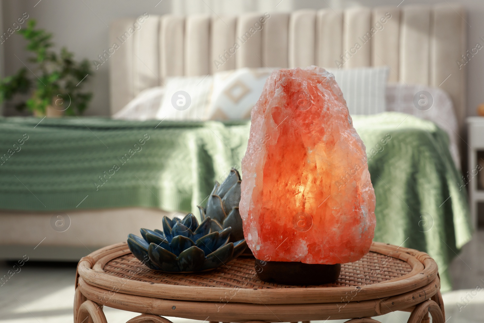 Photo of Beautiful Himalayan salt lamp and lotus figures on wicker table in bedroom