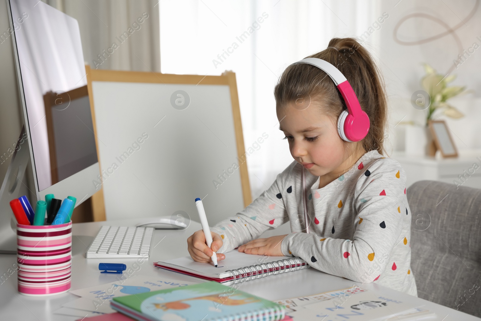 Photo of Little girl learning English indoors at online lesson