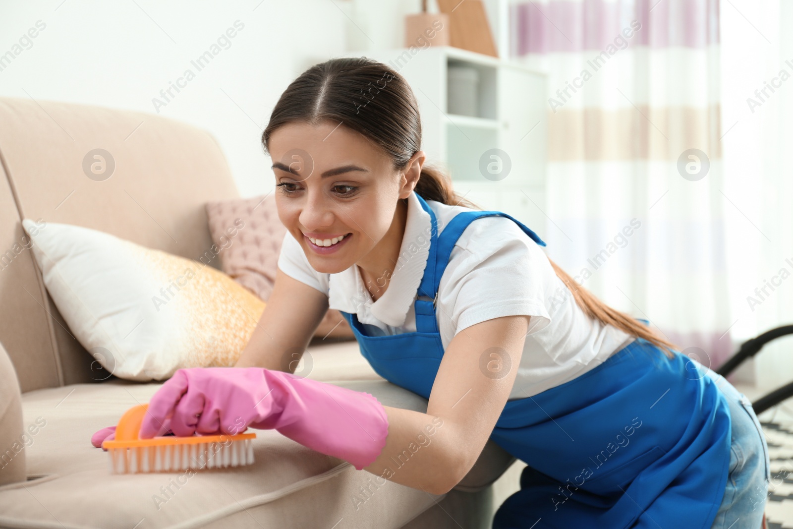 Photo of Portrait of woman cleaning sofa with brush in living room