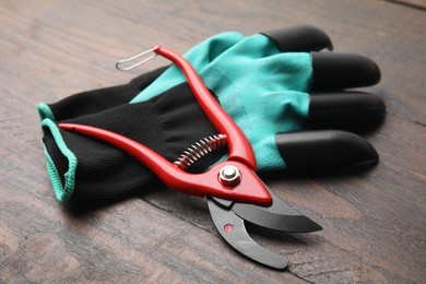 Photo of Pair of claw gardening gloves and secateurs on wooden table, closeup