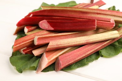 Photo of Many cut rhubarb stalks and leaf on white wooden table, closeup