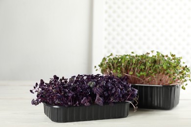 Photo of Fresh radish microgreens in plastic containers on white wooden table, space for text